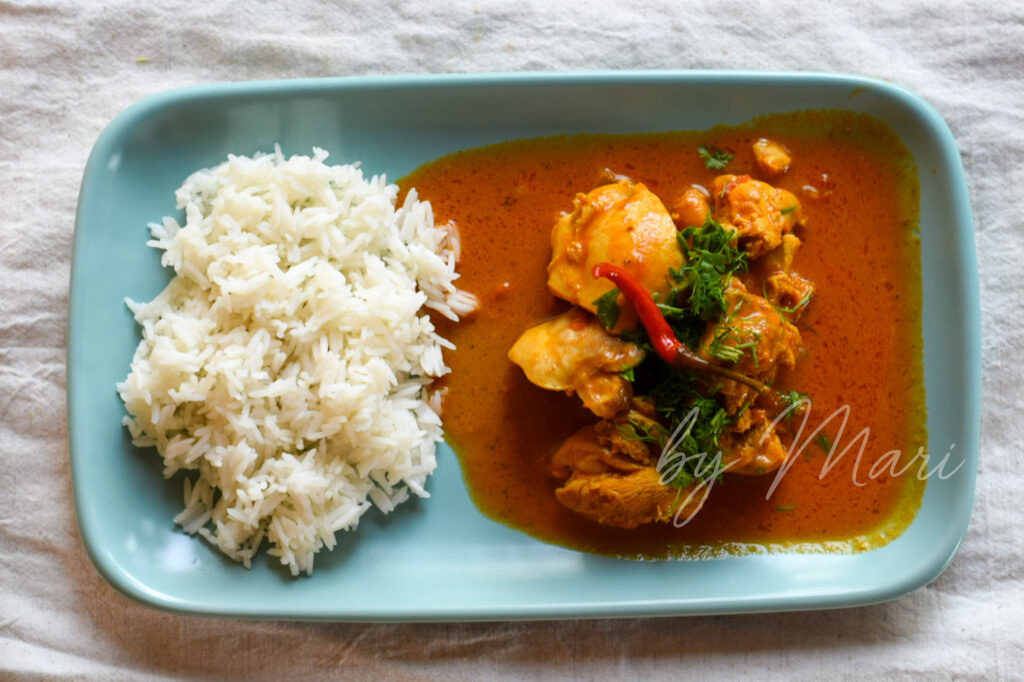 Готовое куриное карри с кокосовым молоком, поданное с рисом и зеленью на тарелке