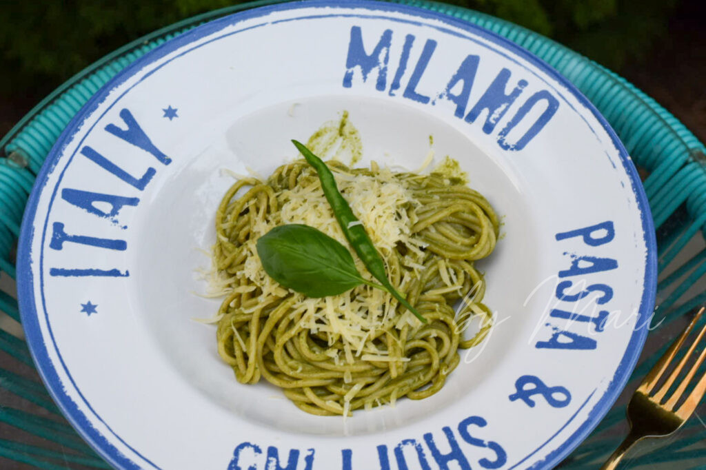 Порция пасты с песто на тарелке, украшенная пармезаном и базиликом